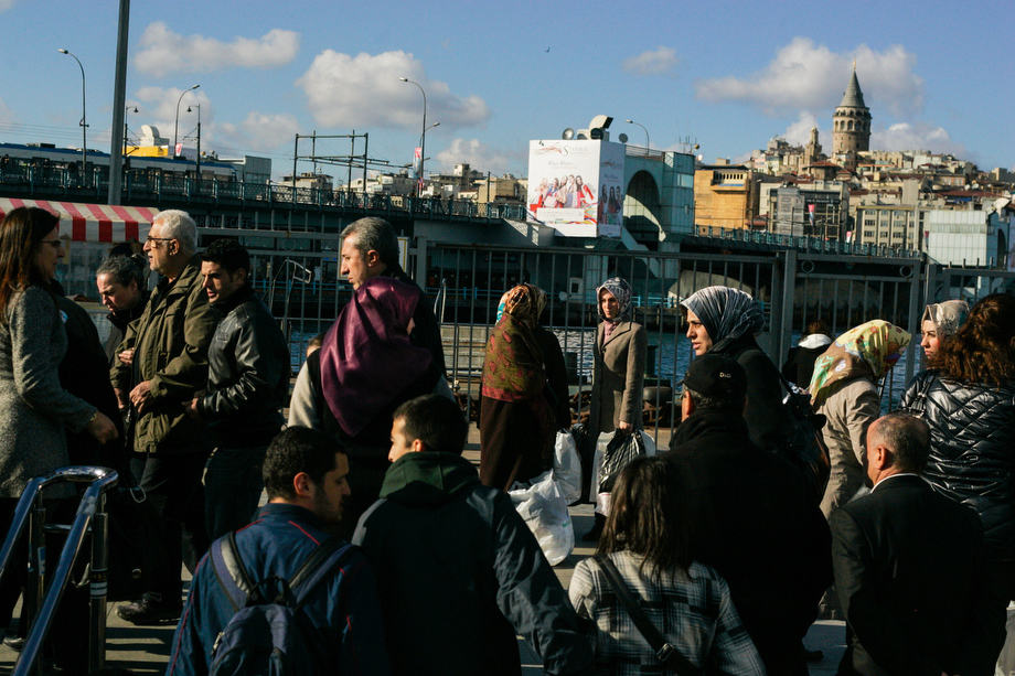 Locals walk by the Boshphorus in Istanbul with the historical Galata Tower in the background.